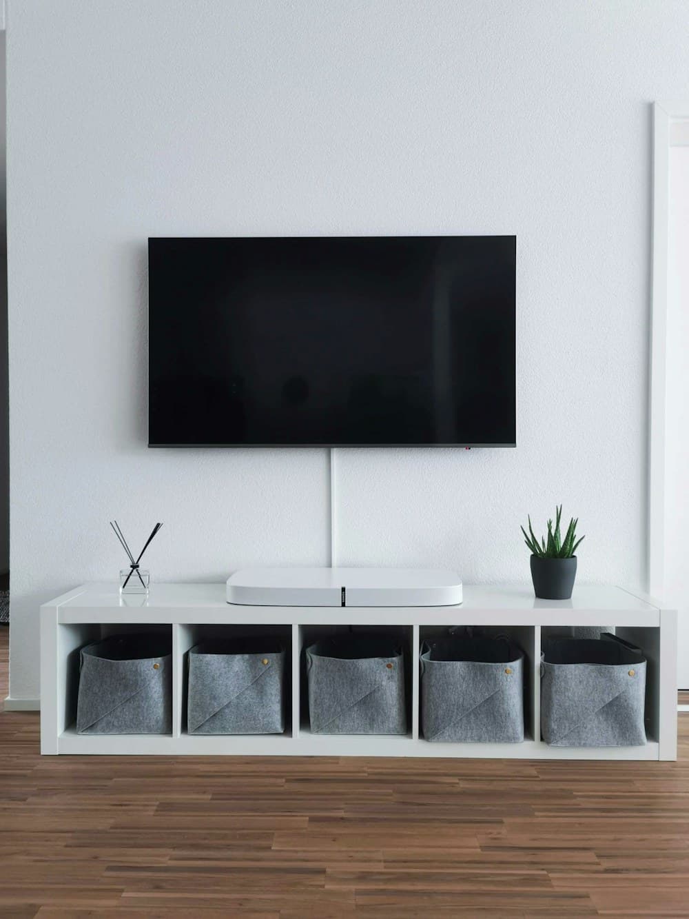 Wall-mounted flat-screen television, switched off, above a low white cabinet