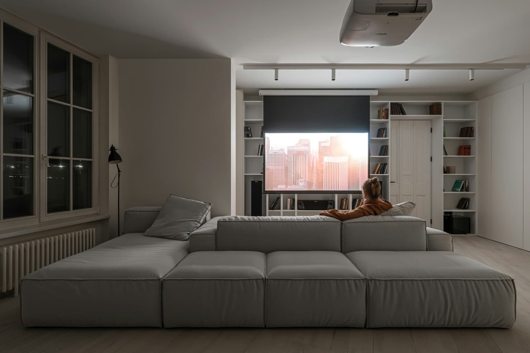 Living room set up for home cinema: a ceiling projector throwing an image onto a screen lowered in front of a sofa